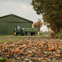 Ein Traktor mit Anhänger steht vor einer Scheune.
